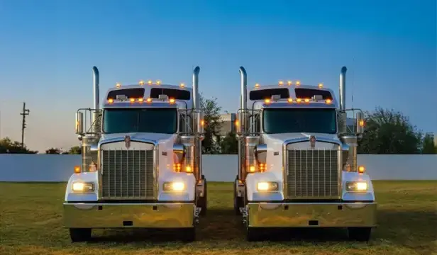 dos tractocamiones clásicos con acabados en cromo, chimeneas de escape altas y luces de posición encendidas al atardecer